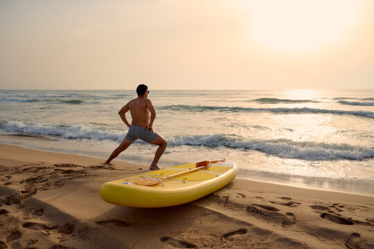 Paddleboarder stretching on the beach at sunrise