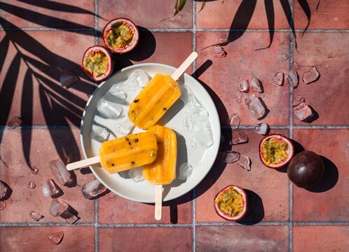 Top view passion fruit popsicles on terra cotta tile in sun.