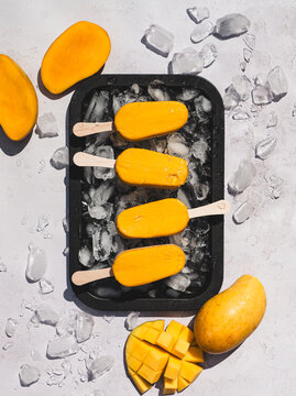 Top view of tray of mango popsicles on white background in sun.