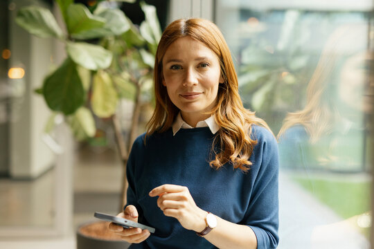 Office worker using mobile phone and looking at camera in a modern setting