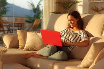 Happy woman at sunset using red laptop at home