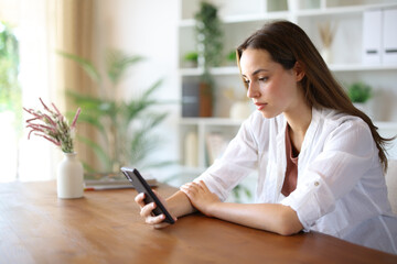 Serious woman checking mobile phone content on a table