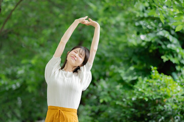 新緑の中で伸びをする女性