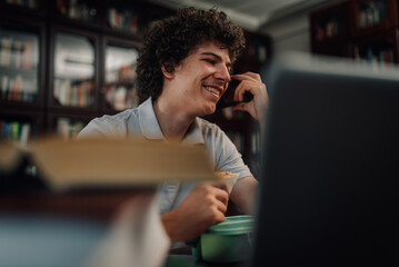 Student eating lunch and talking on phone while studying at home