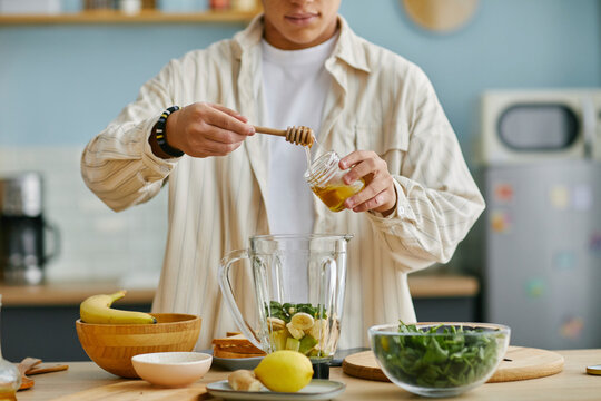 Teenager adding honey to a smoothie in a home kitchen