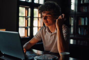 Focused student working on laptop in library, drinking coffee and wearing wireless earbuds