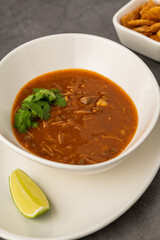 Spicy Mexican chicken soup with noodles, garnished with fresh cilantro and lime wedge