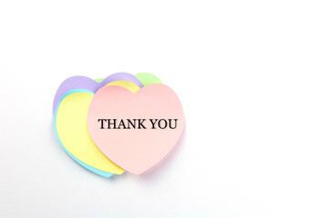 A soft pink heart-shaped sticky note with the word "THANK YOU"  layered over a yellow, blue, and purple heart-shaped sticky notes, on white background. Concept gratitude and appreciation. Top view.