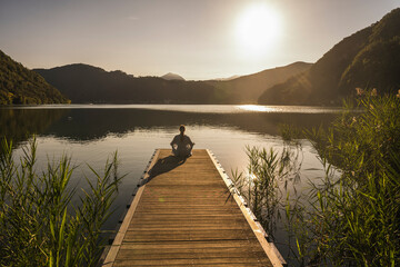 Woman meditating on jetty over lake by mountain range