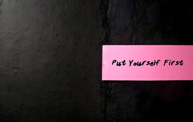 Pink masking tape on black copy space wall  written PUT YOURSELF FIRST -  Prioritize your needs are important as everyone else’s, treat yourself with kindness and set personal boundaries