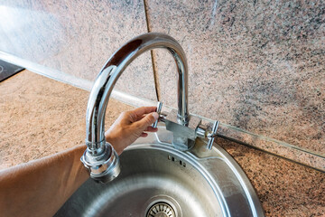 A person skillfully opens a kitchen sink faucet, which is a vital and essential fixture that...