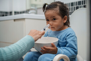 mother making nasal wash for toddler girl with syringe and saline. cleaning nose