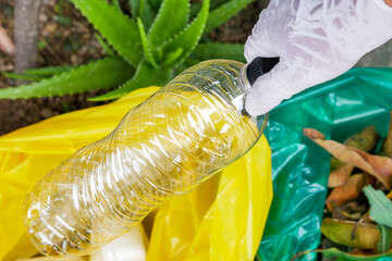Close Up Of Gloved Hand Sorting Waste Places Clear Plastic Bottle Into Yellow Bag For Recycling
