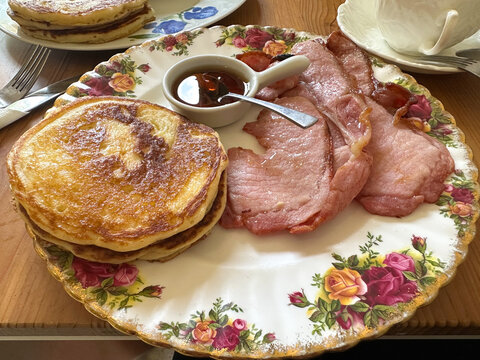Delicious english breakfast plate featuring fluffy pancakes and crispy bacon served with maple syrup on a decorative floral plate, showcasing a delightful morning meal experience - Powered by Adobe