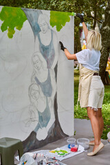 Young adult caucasian female painting mural outdoors in green park. Wearing casual attire and...