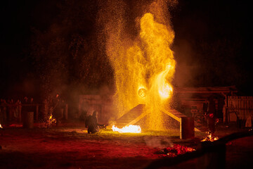 Silhouette of fire performers with sparkling fire staff erupting in night sky, showcasing energy...