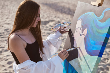 Young female artist paints on canvas at beach, evoking serenity and inspiration. Her artistic...