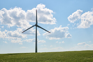 Wind turbine stands tall in lush green wheat field beneath bright blue sky with fluffy white clouds scattered above
