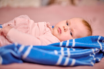 Infant female with red hair and fair skin lies on blue striped blanket. Soft lighting highlights...