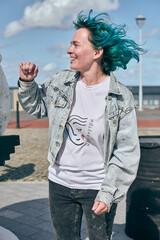 Young woman with blue hair wears denim jacket and white shirt. Standing outdoors with cloudy sky...