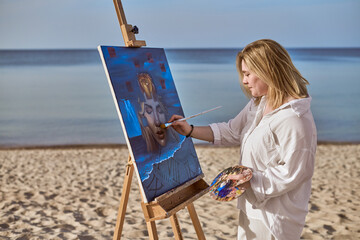 Young woman artist paints vibrant portrait on beach, surrounded by tranquil sea and sky. Her focus...