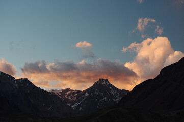 A night view of snowy mountains with clouds at sunset. The clouds and sky turn a magnificent golden color as the sun sets.