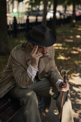Thoughtful man with hat and cane sits on a park bench in autumn sunlight. Concept of lectures on...