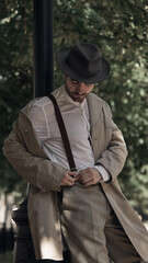 Man in vintage clothing adjusts suspenders outdoors in park. Concept of expressive moodboards for...