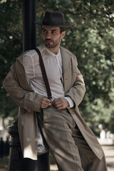 Man in vintage attire leans casually against a lamppost outdoors. Concept of decor imagery for...