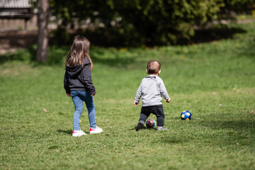 Two young children playing with balls in park on sunny day