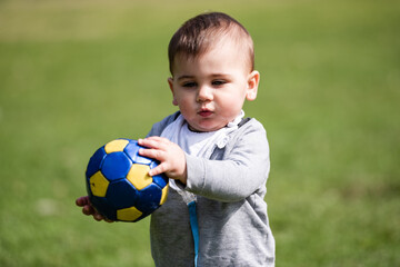 Baby boy holding small soccer ball on grass field