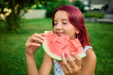 Girl enjoys a slice of watermelon while relaxing in a lush green backyard on a sunny day