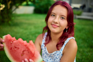 Teen girl enjoying a slice of watermelon in a sunny green park during summer afternoon