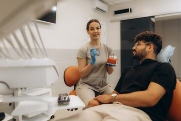 Dentist showing teeth model to patient in modern clinic