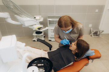 Dentist examining teeth of little girl sitting in dental chair
