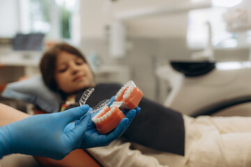 Dentist showing invisible braces on dental mold to young patient