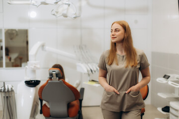 Dentist standing in dental clinic looking away with patient sitting on chair