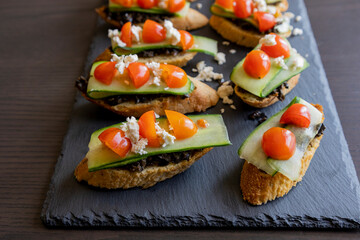 close up stock photo of greek-style crostini topped with olive paste, cucumber slices, cherry tomatoes, and feta cheese