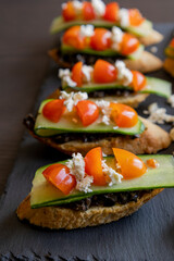 close up stock photo of greek-style crostini topped with olive paste, cucumber slices, cherry tomatoes, and feta cheese