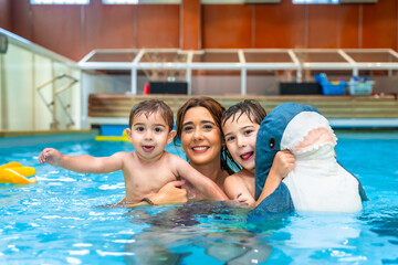 Mother and children playing with plush shark toy in swimming pool