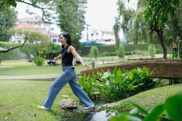 Young woman carefully stepping on rocks crossing a stream in a lush park