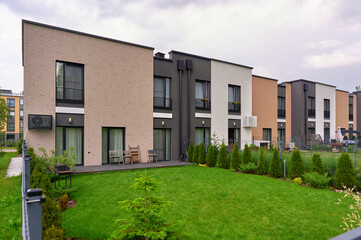 modern townhouse complex with lush green lawn and sleek architecture under cloudy sky, offering urban living and contemporary design appeal. ideal for real estate promotion or architectural showcases