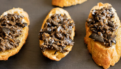 close up stock photo of greek-style crostini topped with olive paste. rustic party appetizer or mediterranean finger food