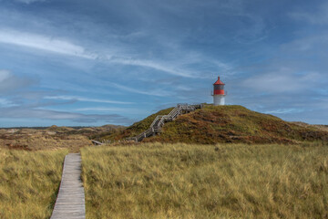 Picturesque Lighthouse on Grassy Hill with Wooden Walkway under Blue Sky