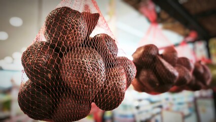 Close-up of snakefruit packed in red mesh bags, hanging in a grocery store display with a blurred background and bright indoor lighting