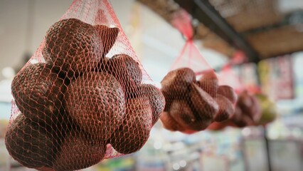 Close-up of snakefruit packed in red mesh bags, hanging in a grocery store display with a blurred background and bright indoor lighting