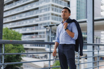Pensive businessman holding eyeglasses and looking up in urban setting