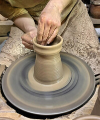 Closeup of clay product being made on pottery wheel. Hands of young craftsman forming clay pot on pottery wheel. Hobbies and creativity.
