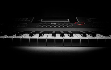 Close-up of an electronic keyboard with dramatic lighting, showcasing black and white keys and...