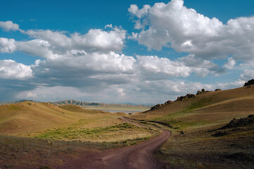 Picturesque landscape with a dirt road in hilly area to Lake Tuzkol, surrounded by mountains. In...